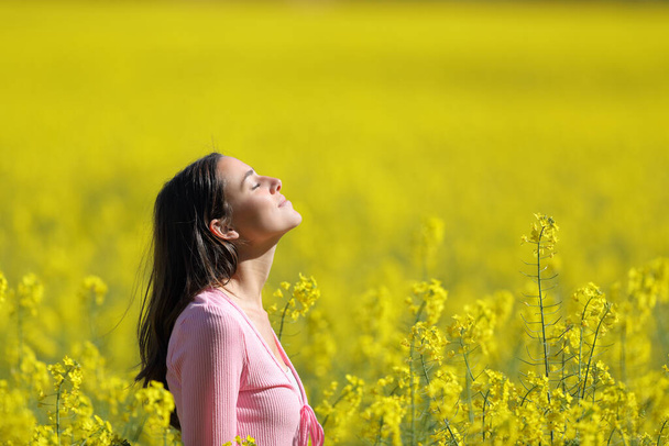 Profile of a relaxed woman breathing deeply fresh air in a yellow field in spring season - Foto, imagen