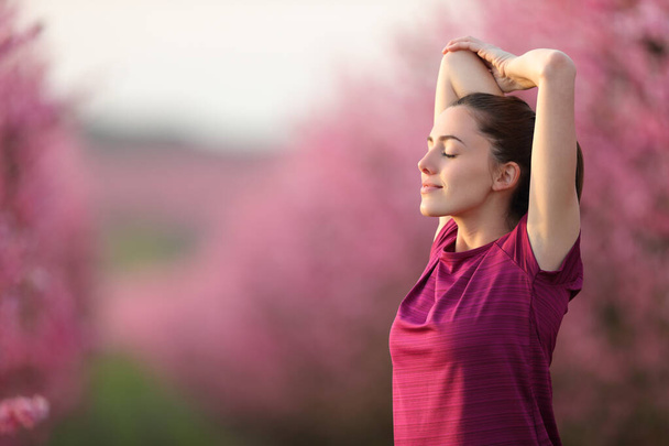 Uvolněný běžec protahuje paže po cvičení v růžovém květovaném poli - Fotografie, Obrázek