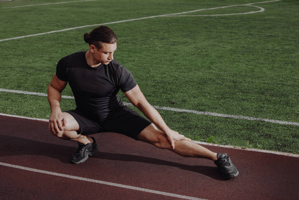 Man stretches leg before running on a stadium - Photo, Image