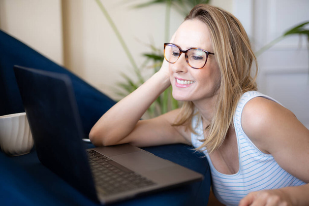 Attrayant jeune femme travaillant sur ordinateur portable et souriant tout en étant assis sur le sol à la maison - Photo, image