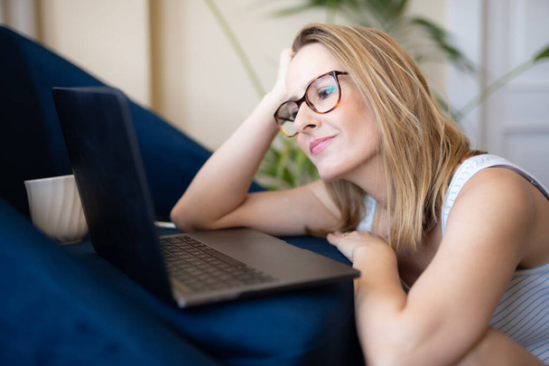 ノートパソコンで働く魅力的な若い女性と笑顔で家の床に座っている間 - 写真・画像