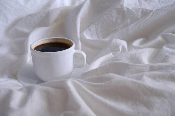 Cup of coffee on white bed linen. - Foto, immagini