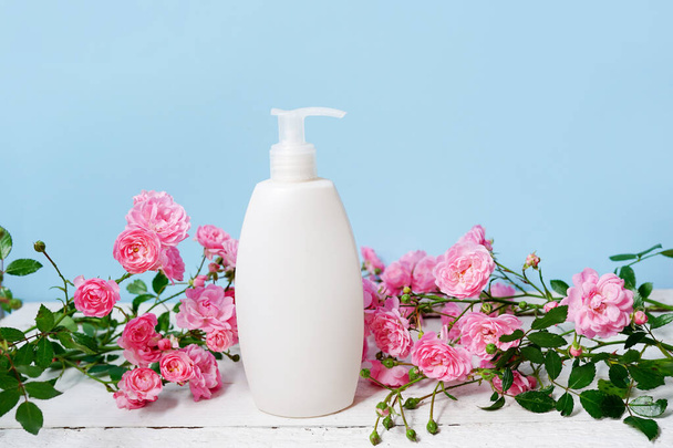 botella con champú o gel de ducha y rosas flores de color rosa sobre fondo azul, productos de cuidado corporal y belleza - Foto, Imagen