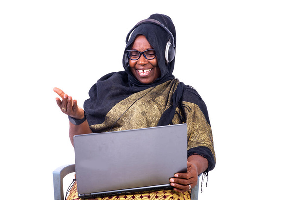 hermosa mujer de negocios musulmana sentada sobre fondo blanco riendo con el ordenador portátil y auriculares. - Foto, imagen