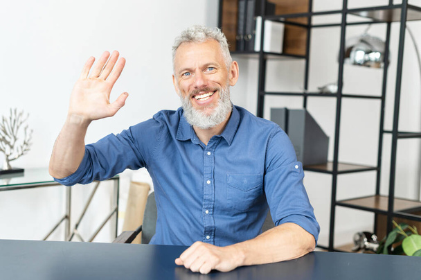 middle-aged male employee looks at the camera and waving hi - Valokuva, kuva