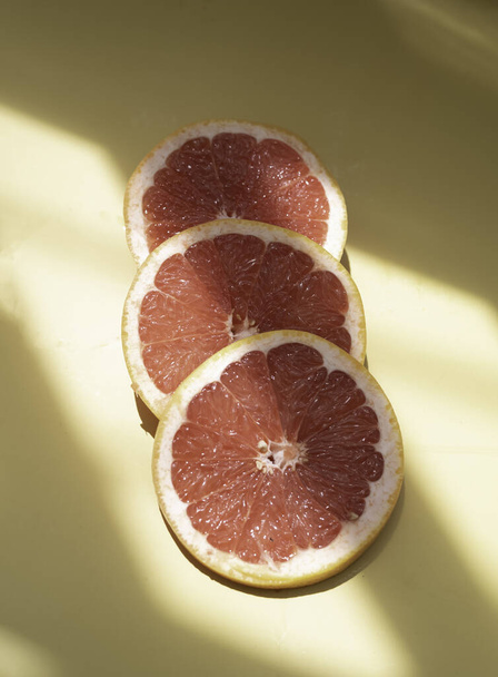 Grapefruitscheiben auf den Hintergrund gelegt, zeigen Fruchtfleisch, Reflexion des Sonnenlichts, das herum scheint - Foto, Bild
