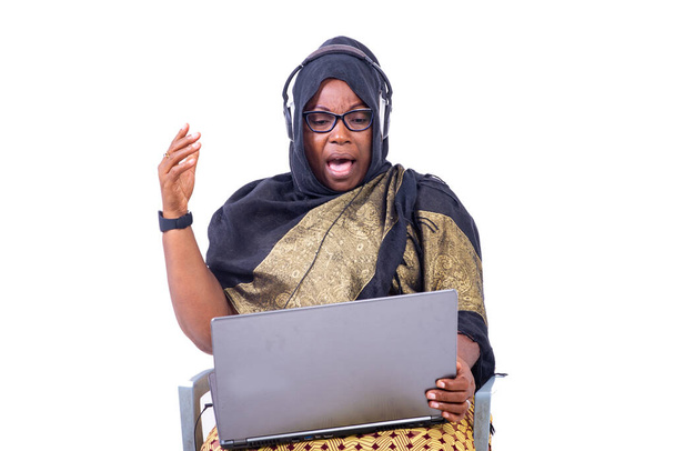 bella donna d'affari musulmana seduta su sfondo bianco che comunica con laptop e cuffie cercando sorpreso. - Foto, immagini