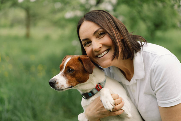 Kobieta gra psa Jacka Russella Terriera na łące. Kobieta przytulająca psa Jack Russell Terrier w naturze. Piękny pies. Kobieta i pies przyjaźni. - Zdjęcie, obraz