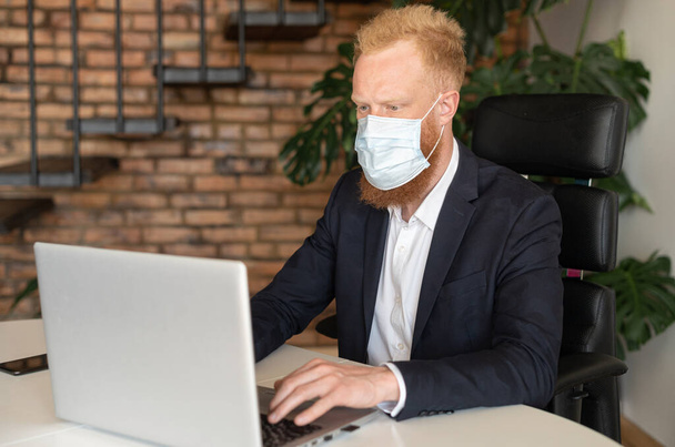 Serious red-haired businessman in smart casual suit wearing protective face mask - Φωτογραφία, εικόνα