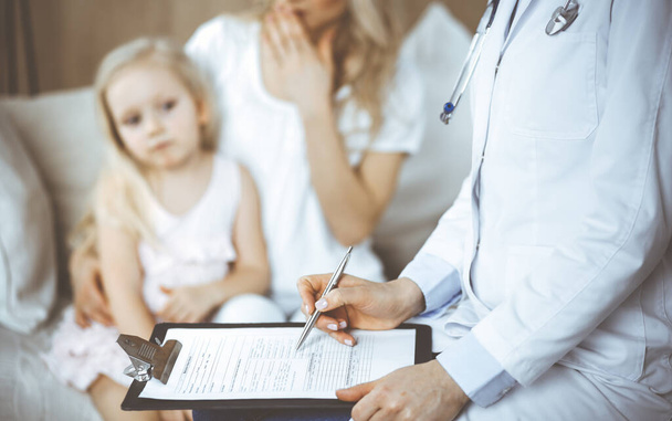 Doctor and patient. Pediatrician using clipboard while examining little girl with her mother at home. Sick and unhappy child at medical exam. Medicine concept - Fotó, kép
