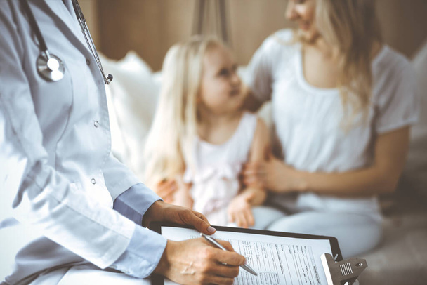 Doctor and patient. Pediatrician using clipboard while examining little girl with her mother at home. Happy cute caucasian child at medical exam. Medicine concept - Fotoğraf, Görsel
