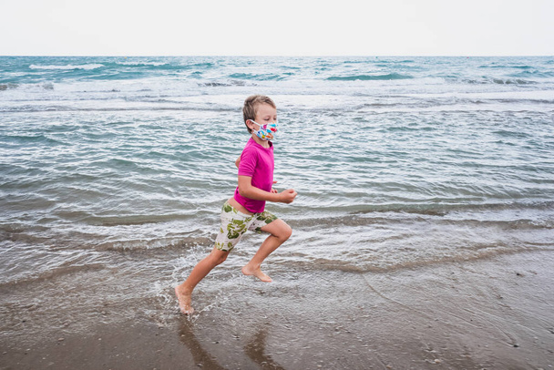Retrato de un niño en la playa con una máscara protectora contra virus en vacaciones. - Foto, imagen