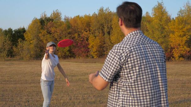 Мужчина и женщина играют, бросают друг другу красный диск в парке. Беззаботная пара, молодые люди веселятся вместе. Спорт и молодость. Счастливая семья играет в парке, дочь и отец - Фото, изображение