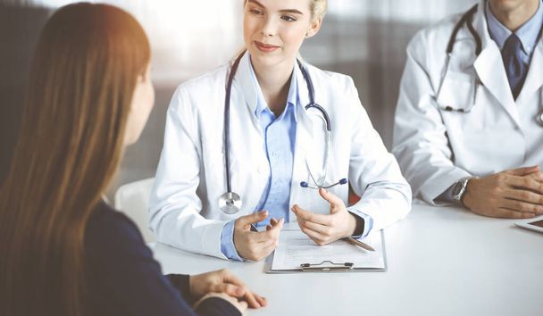 Woman-doctor with male colleague are consulting patient woman while sitting at the desk in modern clinic. Perfect medical service, medicine concept - Photo, image