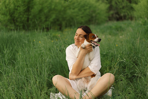 Kadın çayırda Jack Russell Terrier 'cilik oynuyor. Jack Russell Terrier köpeğine sarılan bir kadın. Güzel köpek. Kadın ve köpek dostluğu. - Fotoğraf, Görsel