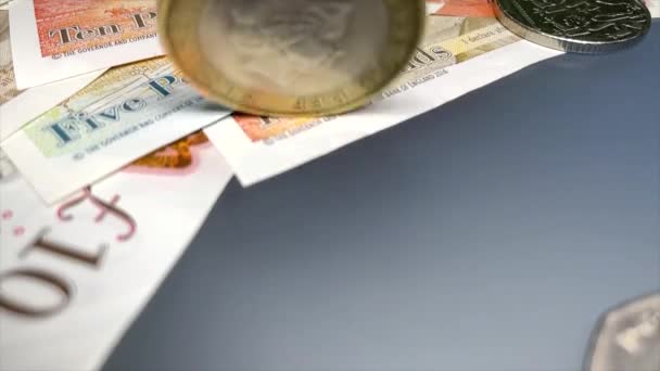 Brit 2 fontos érme lassított felvételben egy halom font sterling bankjegyen. Egyesült Királyság pénzügyi rendszer, fenntartható gazdasági növekedés. Angol font, mint vezető nemzetközi valuta. A font árfolyam ingadozása. Brit pénz. 4K 3840x2160 - Felvétel, videó