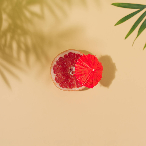 Parlak kırmızı şemsiyeli greyfurt açık sarı arkaplanda ve palmiye yaprakları gölgeli. Yaz tatili plaj konsepti. Düz yatıyordu. - Fotoğraf, Görsel