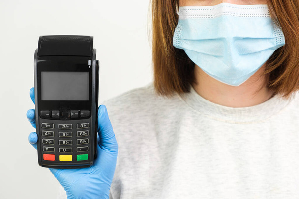 ゴム手袋とフェイスマスクの女性は、コロナウイルスのパンデミックの間に支払いのためのPOS端末を保持 - 写真・画像
