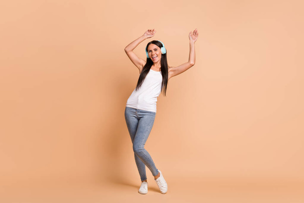 Full length photo portrait of girl in earphones dancing isolated on pastel beige colored background - Фото, изображение