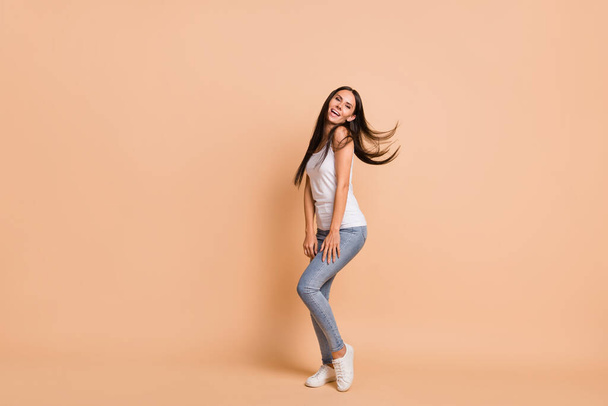 Full size profile photo of optimistic brunette girl dance sing wear white top jeans sneakers isolated on beige background - Φωτογραφία, εικόνα