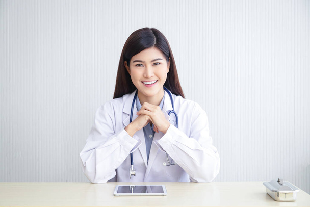 Прекрасний азіатський лікар сидить за своїм столом у офісі. Концепція медичних послуг у лікарнях Лікування та охорона здоров'я пацієнтів. - Фото, зображення