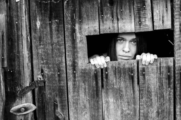 Een vrouw die door de scheur van een afgesloten houten schuur kijkt. Zwart-wit foto. - Foto, afbeelding