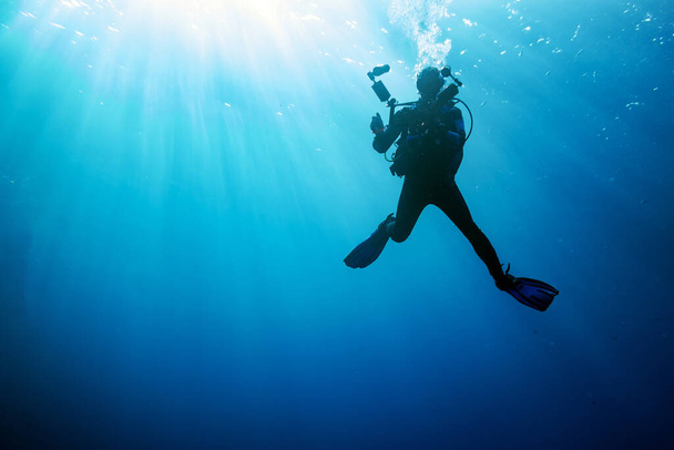 potápěč s vybavením pro podvodní natáčení pod vodou na modrém pozadí  - Fotografie, Obrázek