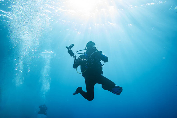 водолаз з обладнанням для підводного зйомки під водою на синьому фоні
  - Фото, зображення