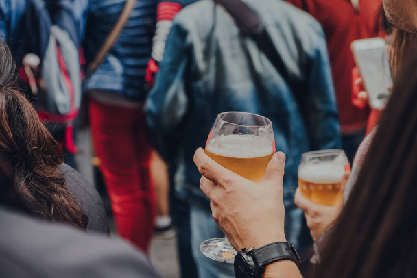 Mãos femininas segurando copos de cerveja em uma rua, foco seletivo em primeiro plano. - Foto, Imagem