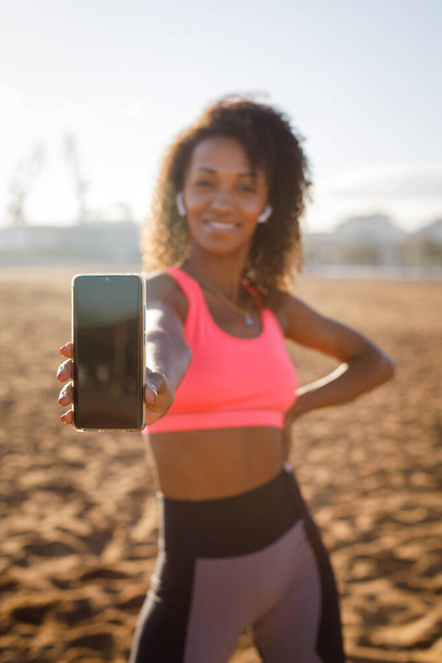 Fitt sportos nő mutatja az okostelefon képernyőjét. Fitness és futás edzés app koncepció. - Fotó, kép