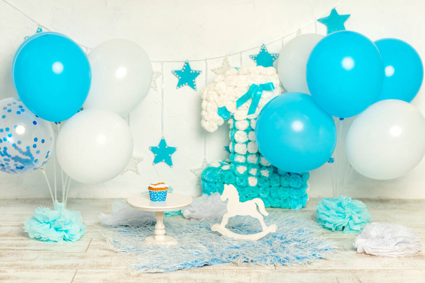 ontwerp van de fotozone voor de verjaardag van een 1-jarige jongen in het blauw met ballonnen en een taart, het concept van de vakantie en decor - Foto, afbeelding