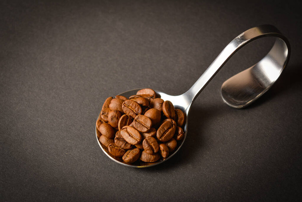 Top view of Roasted coffee beans served in silver vintage stainless steel spoon on dark background. High quality organic aroma seeds. Copy space text image - Foto, Imagem