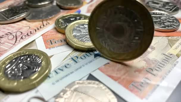 Britská dvoulibrová mince se točí na hromadě librových bankovek. Britský finanční systém. Britská libra, mezinárodní měna. Kolísání směnného kurzu. Britské peníze. 4K video 3840x2160 - Záběry, video