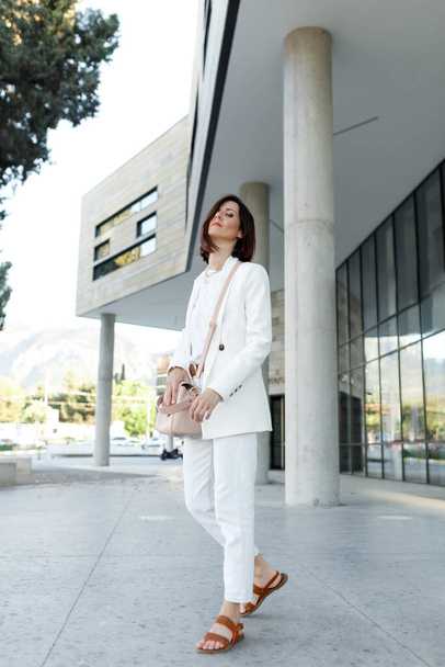 Schöne Millennial stilvolle Hipsterfrau mittleren Alters posiert draußen in weißen Kleidern. Erfolg im Geschäftsviertel, Kopierraum - Foto, Bild