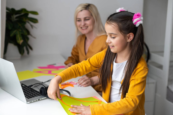 Söpö pieni peruskoulun tyttö tekee origami kala taitettu väri paperi näköinen video kannettavan tietokoneen, online-työpaja, lapset kotona toimintaa, luovuutta ja etäopetusta. - Valokuva, kuva