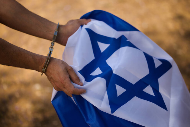 Detalle de las manos encadenadas agarrando una bandera de Israel. Represión de la población palestina. - Foto, imagen