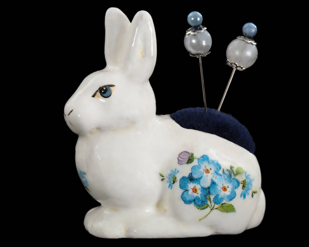 Porselen bir tavşan heykeli, dikiş için iğne yatağı, siyah arka planda izole edilmiş. - Fotoğraf, Görsel
