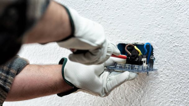 Electrician worker with screwdriver fixes electrical cables in the terminals of the socket of an electrical system. Working safely with protective gloves. Construction industry. - Фото, зображення