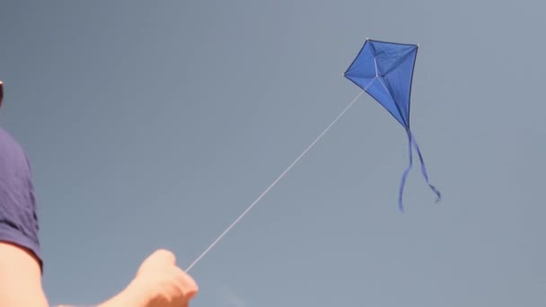 Blauwe vlieger zweeft in de blauwe lucht. Man regeert vlieger. Het concept van vrijheid, zomerhobby 's, entertainment in de natuur. Minimalisme, ruimte voor tekst, tinten blauw.  - Video