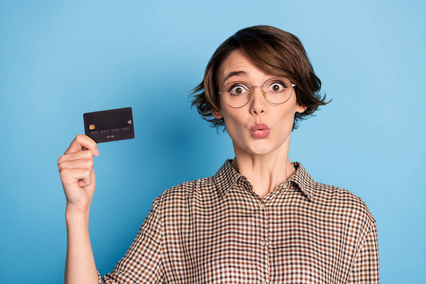 Portrait of shocked person hand hold debit card staring camera wear checkered isolated on blue color background - 写真・画像