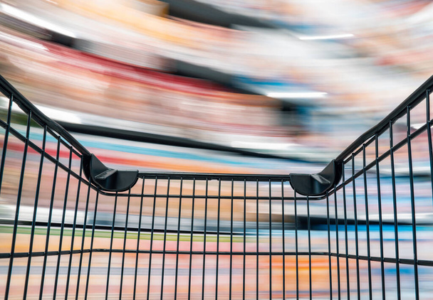 Leeg zwart winkelwagentje met beweging in het gangpad van de supermarkt, klant kiest product op de markt plank winkel - Foto, afbeelding