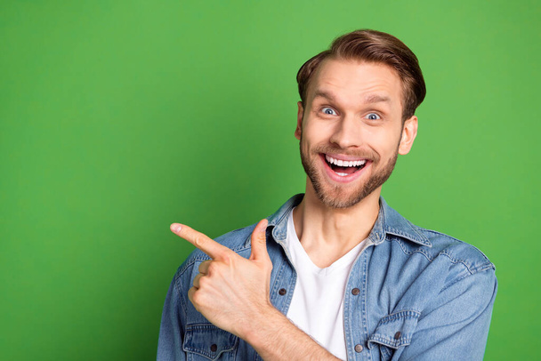 Photo portrait of amazed guy pointing blank space surprised smiling isolated on vibrant green color background - Foto, Imagem