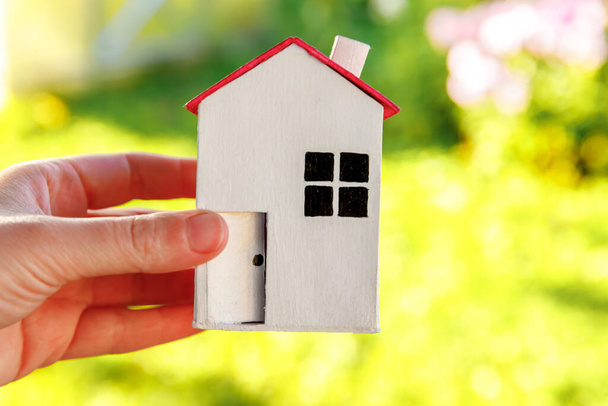 Miniaturowy model domu w kobiecej dłoni na zielonym tle zewnętrznym. Eco Village, abstrakcyjne środowisko. Nieruchomości hipoteczne ubezpieczenie nieruchomości sen dom ekologia koncepcja - Zdjęcie, obraz