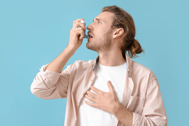 Junger Mann mit Inhalator hat Asthmaanfall vor farbigem Hintergrund - Foto, Bild