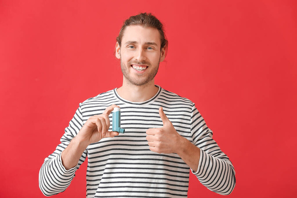 Young man with inhaler showing thumb-up on color background - Foto, Imagem