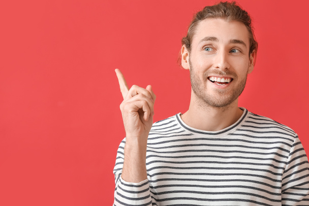 Smiling young man pointing at something on color background - Photo, Image