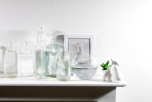 A set of water bottles of different shapes with a photo frame and a pot with artificial succulent is on the dresser. Copy space - Фото, зображення