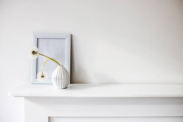 A corrugated vase in the style of the seventies with two fluffy dandelions in the background of a photo frame is on the dresser. Space for text. - Foto, imagen