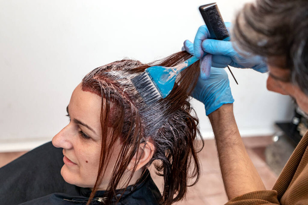 Mains de coiffeur teindre les cheveux de la cliente avec un pinceau au salon de beauté. Appliquer la couleur des cheveux avec le pinceau. Concentration sélective. - Photo, image