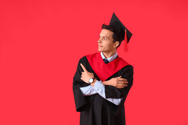 Male graduating student pointing at something on color background - Фото, зображення